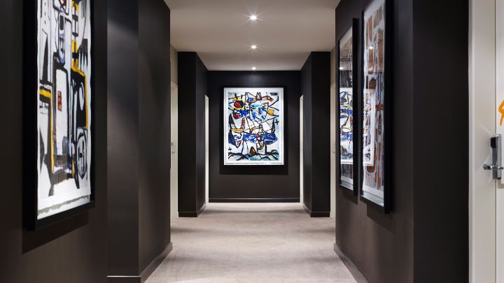 Hotel hallway with cream carpet, charcoal walls, and colourful paintings